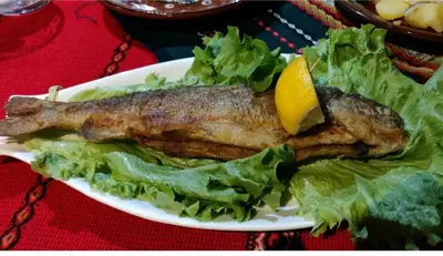 a plate of fish with lettuce and a lemon on it at Къща за гости Динас in Zmeitsa