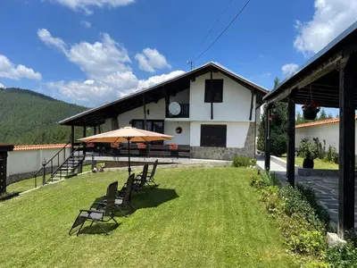 a house with chairs and an umbrella in the yard at ПАУНОВАТА КЪЩА in Yasă-Koriya