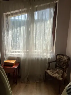 a window with white curtains and a chair and a table at Guest House Kalina in Sapareva Banya