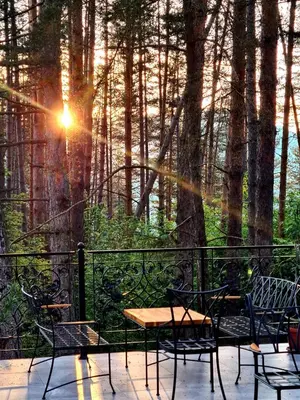 a table and chairs on a deck with the sun shining through the trees at Вила АРБОРЕТУМ - онлайн self check-in in Teteven