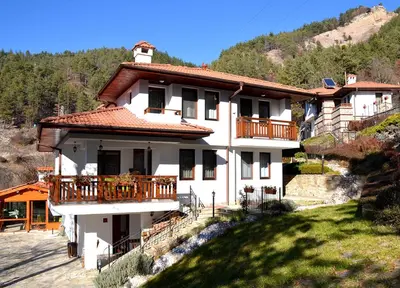 a white house with a balcony on a hill at Къщи за гости 