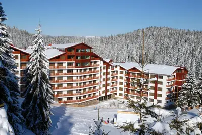 a large building in the snow with snow covered trees at Апартамент DIMANI-Апартхотел Форест Нук Пампорово in Pamporovo