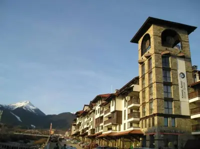 a building with a clock tower with a mountain at Bansko Royal Towers - Studio 945 in Bansko