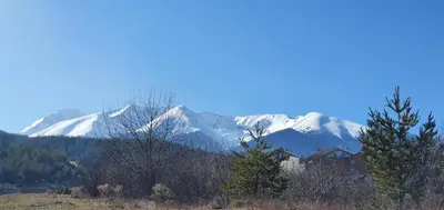 a snow covered mountain range with trees and a house at Луксозно студио в Банско - малко кътче от рая. in Bansko