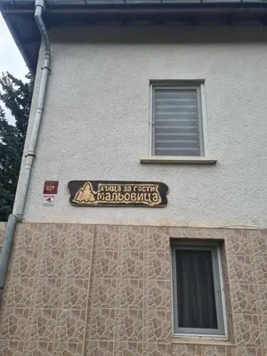 a sign on the side of a building with two windows at Мальовица - къща за гости in Dospey Makhala
