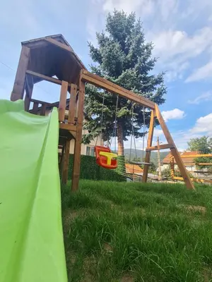 a wooden play structure in the grass with a slide at Мальовица - къща за гости in Dospey Makhala