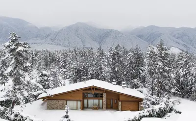 a log cabin in the snow with mountains in the background at Luxury Chalets Pirin Golf & Country Club in Bansko