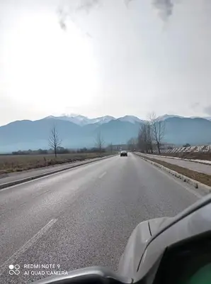 a car driving down a highway with mountains in the background at Апартамент-студио в Банско-Разлог,Aspen Golf- C206 in Bansko