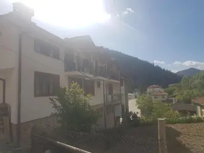 a white house with a hill in the background at Къща за гости Камината in Trigrad