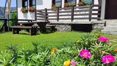 a garden with a bench and flowers in front of a house at Авина къща in Kovachevitsa