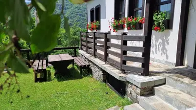 a wooden bench next to a building with flowers in a window at Авина къща in Kovachevitsa