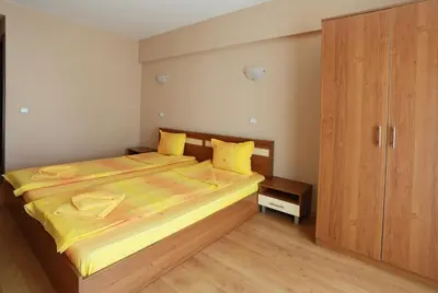 a bedroom with a bed with yellow sheets and a wooden cabinet at Acropolis Hotel in Pazardzhik