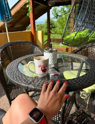 a woman with red nail polish sitting at a table with a cup of coffee at Sunshine villa Dzhigurovo in Sandanski