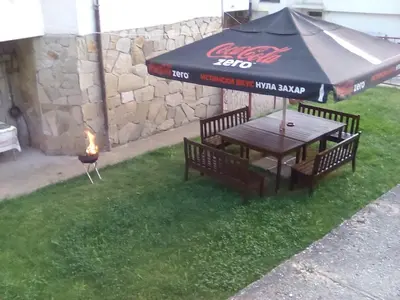a picnic table with an umbrella and a fire in the grass at Katya Guest House in Smolyan