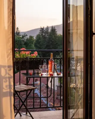 a table with a bottle of wine and glasses on a balcony at Family Hotel Konstantinovi in Kyustendil