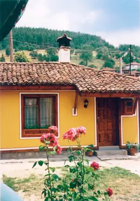 a small yellow house with a chimney and flowers at Янко Кехая in Koprivshtitsa
