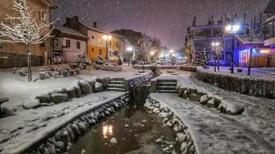 a snow covered city street with a pond and benches at Private Spa Luxury apartments in Bansko