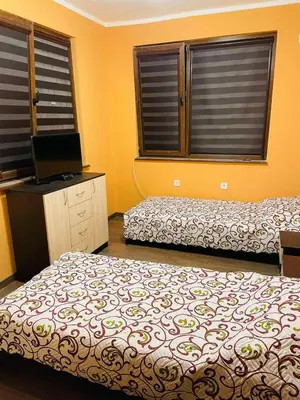 a bedroom with two beds and a television and two windows at Къща за гости Станеви in Ribarica