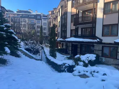 a snow covered yard in front of a building at Bardarova Apartments Downtown Bansko in Bansko