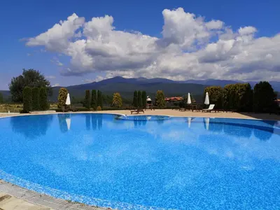 a large blue swimming pool with chairs and umbrellas at Студио за трима, басейн, Aspen Golf Resort, Банско, Разлог in Razlog