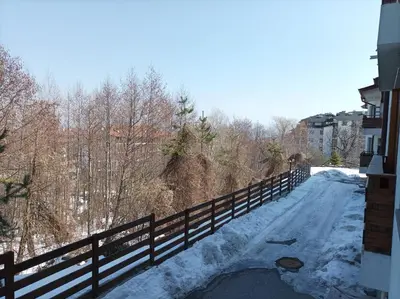 a snow covered road with a fence and trees at Apartment Detelina Residence in Bansko
