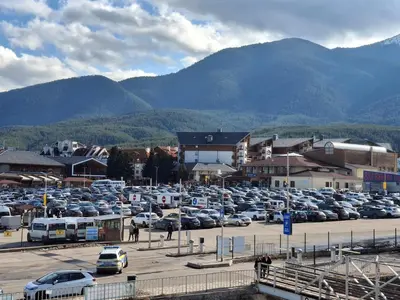 a parking lot filled with parked cars in front of mountains at Илен 433 Bansko Royal Towers in Bansko