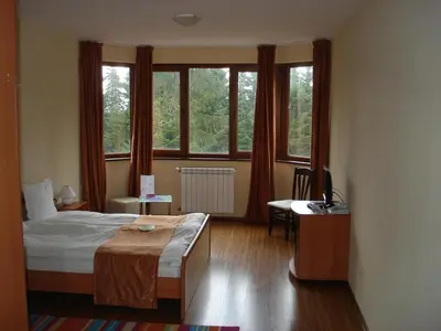 a bedroom with a bed and a desk and windows at Стаи и апартаменти под наем in Borovets