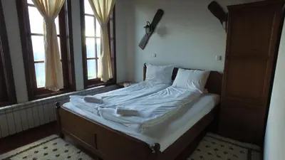 an unmade bed in a room with two windows at Leshtenski Rai Guest House in Leshten