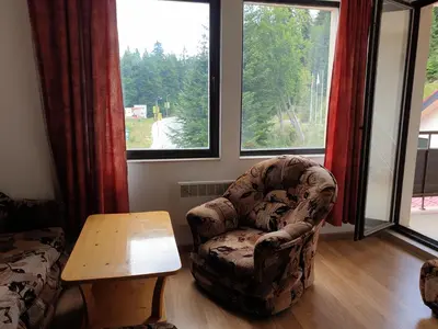 a living room with a chair and a table and windows at Снежанка in Pamporovo