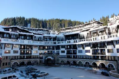 a large building with a parking lot in the snow at Гранд Манастира Частен Апартамент in Pamporovo