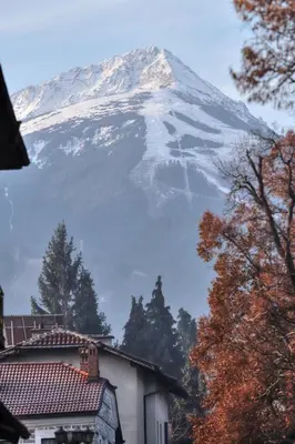a snow covered mountain in front of a house at Ground floor 2-bedrooms, 2-bathrooms apartment near Bansko in a complex with pools and SPA included in Razlog