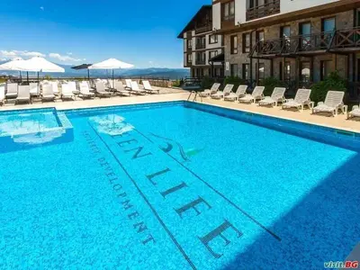 a large blue swimming pool with chairs and a building at Студио Snow day в Green life в Банско in Bansko