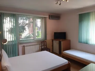 a room with two beds and a tv and two windows at Hotel Tsarevets in Asenovgrad