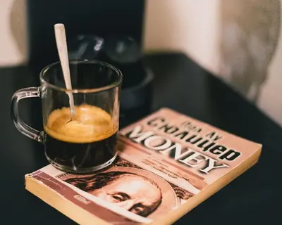 a cup of coffee and a book on a table at HIDDEN BANK: First Million in Plovdiv