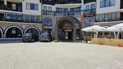 a parking lot in front of a building with umbrellas at Апартамент Amare, Гранд Манастира in Pamporovo