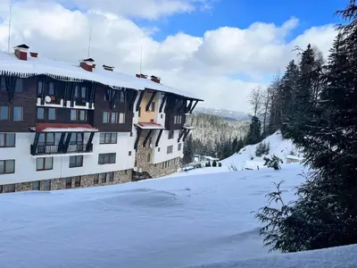 a building with snow on the ground in front of it at Апартамент Amare, Гранд Манастира in Pamporovo