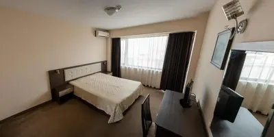 a room with a bed and a table and a television at Хотел България Петрич in Petrich