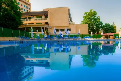 a swimming pool with chairs and umbrellas in front of a building at Хотел България Петрич in Petrich
