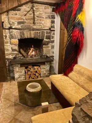 a living room with a stone fireplace and a couch at Къща Александрова с басейн вътрешен и отопляем in Arda