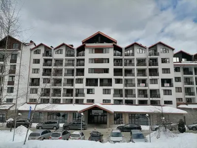 a large white building with cars parked in a parking lot at Petkovi Аpartments, Borovets Gardens - One-bedroom and Two-bedroom apartments in Borovets