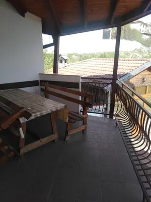 a porch with a table and benches on a balcony at Вила Родопи in Dospat