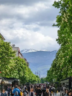 a crowd of people walking down a street with mountains in the background at Top Center Relax, NDK & Vitoshka & Metro station in Sofia