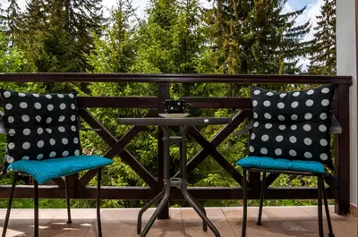 two chairs and a table on a balcony with trees at Stand'Art - апартамент , Смолянски езера in Smolyan