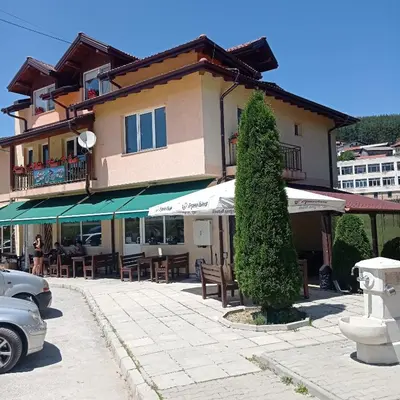 a building with tables and umbrellas in a parking lot at Къща за гости-Ганеви in Zmeitsa
