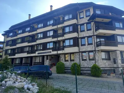 a large building with cars parked in front of it at Bansko All Seasons - Cozy Apartments Near Gondola & Mountain Views in Bansko