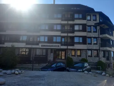 a building with two cars parked in front of it at Bansko All Seasons - Cozy Apartments Near Gondola & Mountain Views in Bansko