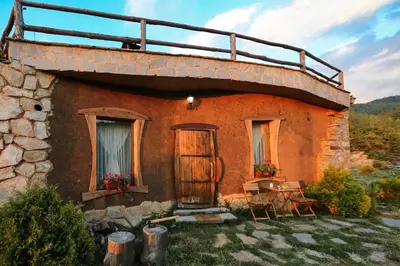an old stone house with a table and chairs at Панорама хаус Лещен и еко къщи Дървена и Землянка in Leshten