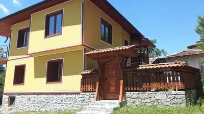 a yellow house with a wooden deck and a building at Къща за гости Феникс in Koprivshtitsa