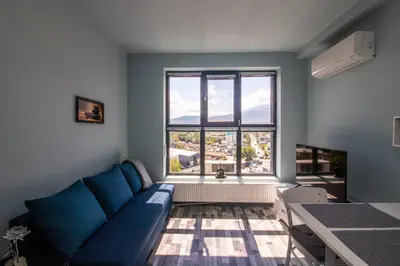 a living room with a blue couch and a large window at Mountain View Apartment 1 + Parking in Sofia