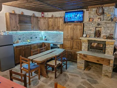 a kitchen with a wooden table and a stone fireplace at Къща за гости Близнаците in Leshten